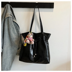 Détail du sac cabas en cuir verni noir avec nœud coulissant et charm en peluche