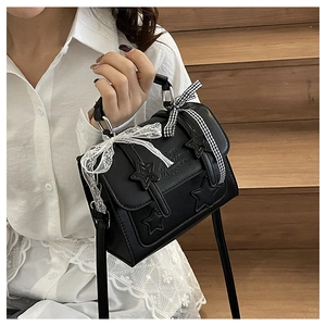 Close-up of black messenger bag with star pattern, white lace bow and checkered ribbon
