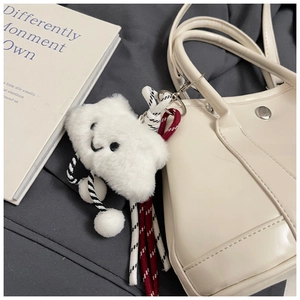 Detail of a white fluffy cloud keychain with embroidery hanging on a leather handbag