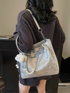 Silver snakeskin tote bag with pearl chain and plush charm shown on a shoulder