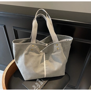 Detailed close-up of grey canvas tote bag with cream straps and golden rivet accents