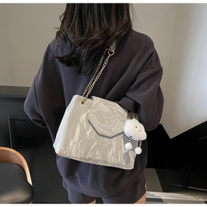 Detail of grey pleated leather bag with gold chain and plush cloud charm on shoulder
