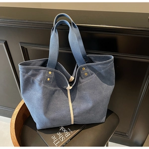 Detail of blue canvas tote bag showing white webbing and gold metal rivet reinforcements