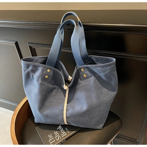 Detail of blue canvas tote bag featuring contrast white stitching and metal rivets