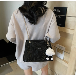 Detail of black pleated shoulder bag with gold chain strap and plush cloud charm