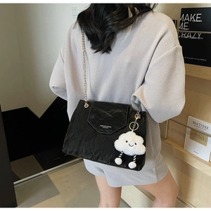 Detail of black pleated shoulder bag with gold chain strap and plush cloud charm