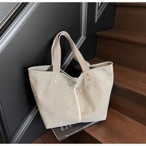 Detail of light grey tote bag with metallic studs on a dark wooden background