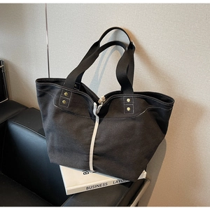 Close-up of black canvas tote bag with contrast stitching and brass rivet details
