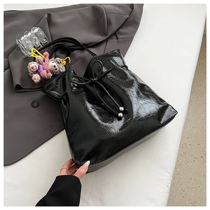 Détail d'un sac cabas noir brillant plissé avec un pendentif ours en peluche marron