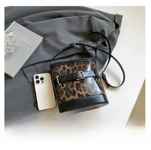 Leopard print bucket bag with black strap and metallic buckle detail on flat lay surface