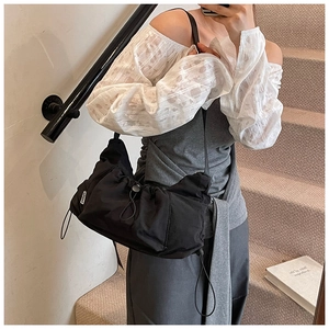 Detail of black nylon tote bag featuring drawstring pleats and side brand label
