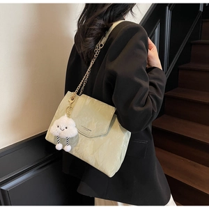 Detail view of a light green pleated leather bag with gold chain and plush charm