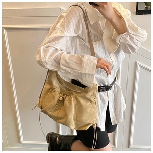 Detail of beige pleated nylon tote bag featuring a front pocket and drawstring closure