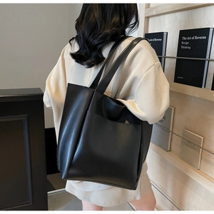 Detail of black tote bag with shoulder straps and front pocket shown on model