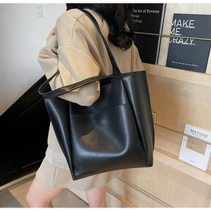 Detail of a black leather tote bag with a front pocket shown on a model in a library