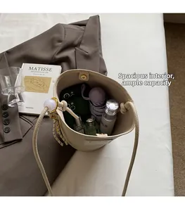 Intérieur spacieux d'un sac seau en cuir beige contenant téléphone, parapluie et cosmétiques