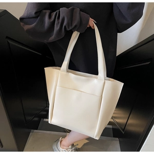 Detail of a cream-colored leather tote bag featuring a practical front outer pocket