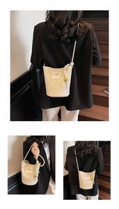 Détail du sac seau en cuir crème avec cordon tressé et pendentifs dorés
