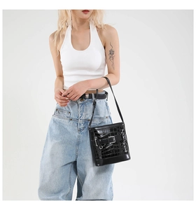 Détail d'un sac à bandoulière noir effet crocodile avec boucle décorative et fine lanière