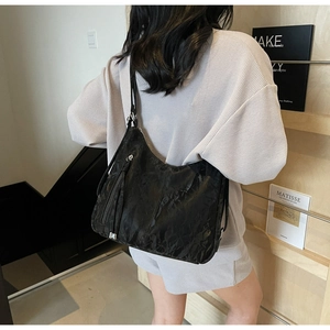 Detail of black pleated shoulder bag with long tassel zippers and silver hardware finish
