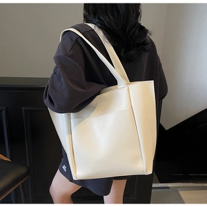 Minimalist off-white faux leather tote bag with large front pocket on model's shoulder