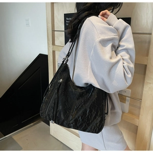 Side view of black wrinkled leather tote bag with long tassels and silver metal hardware