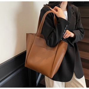 Close-up of brown leather tote bag with large pocket worn with a black blazer