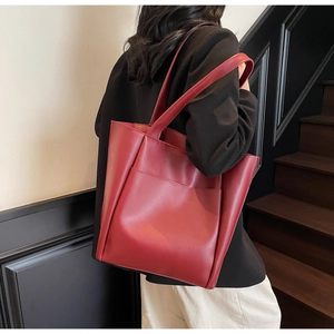 Detail view of burgundy leather tote bag featuring a large front pocket and long handles