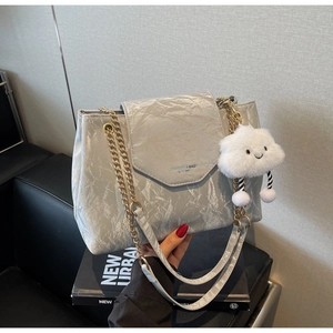 Silver-grey pleated shoulder bag with gold chain and cloud charm on a black book