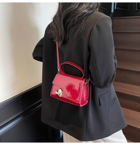 Mini borsa in pelle verniciata rossa con fibbia a cuore argento indossata su blazer nero