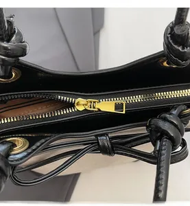 Close-up of smooth gold zipper detail and knotted handle on black glossy bucket bag