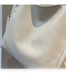 Close-up of beige leather shoulder bag showing natural grain texture and precise side stitching