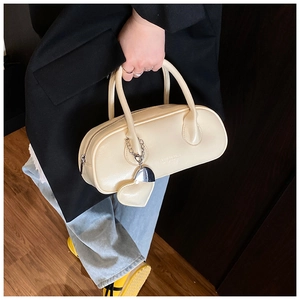 Détail d'un sac bowling crème avec texture litchi et breloque cœur porté par un mannequin