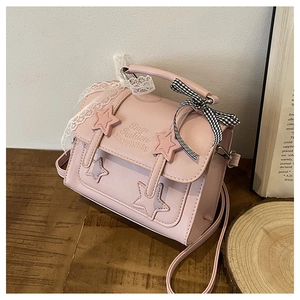 Close-up of pink messenger bag with star appliques and lace bow detail on a wooden table