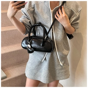 Détail du sac cylindrique noir brillant avec breloque cœur et bandoulière réglable