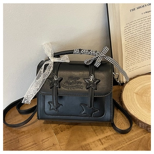 Detail of black star crossbody bag with bow ribbons on handle on wooden table