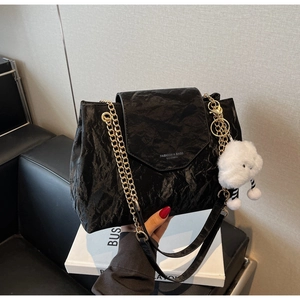 Detail of black wrinkled leather shoulder bag with gold chain and plush cloud pendant
