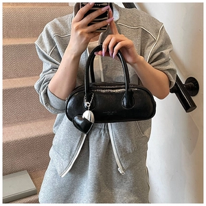 Détail du sac bowling noir brillant avec un pendentif en cœur et texture gaufrée