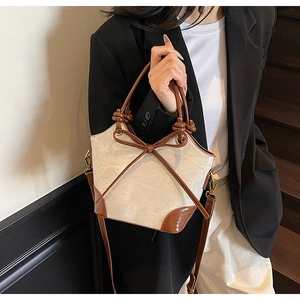 Detail of a beige canvas bucket bag with brown leather trim and bow decoration