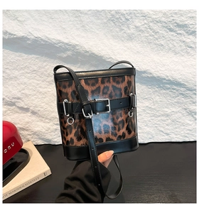 Détail du sac seau à imprimé léopard brillant avec bordures et sangles en cuir noir