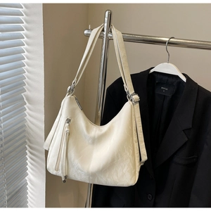 Detail of cream white faux leather tote bag showing side tassel zipper and textured finish