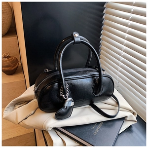 Détail d'un sac bowling noir brillant avec pendentif cœur et texture cuir froissé