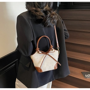 Detail of a chic cream bucket bag with brown leather trim and a front bow accent