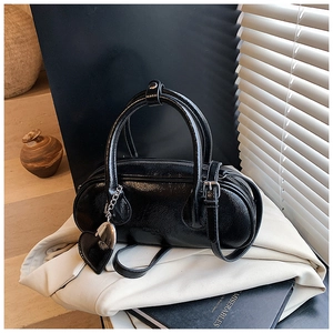 Détail d'un sac bowling cylindrique noir brillant avec breloque cœur et bandoulière