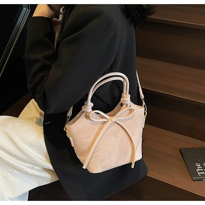 Detail of a pink crossbody bucket bag featuring a large bow and woven handle details