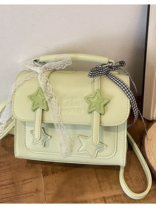 Light green messenger bag with star buckles and decorative ribbons on wood surface