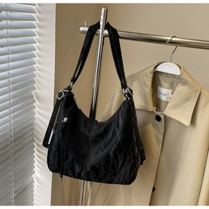 Detail of black tote bag with pleated texture and silver hardware on a metal hanger