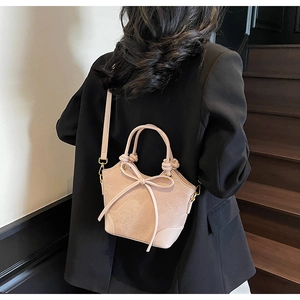 Crossbody view of light pink bucket bag with bow detail and golden metal hardware