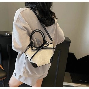 Detail of a two-tone bucket bag with black round handles and bow on a crossbody strap