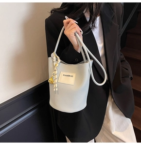 Détail du sac seau bleu clair avec texture grainée, étiquette et perle dorée décorative